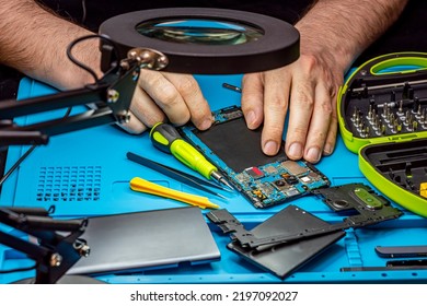 Smartphone Repair In A Service Center. Hands Of A Professional Master Repairman Repairing Disassembled Into Pieces Cell Phone. Internal Parts, Chips, Motherboards, Wiring, Fixing Process.