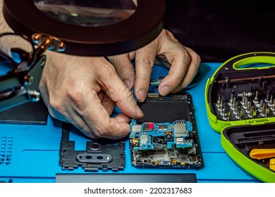 Smartphone Repair In A Service Center. Hands Of A Professional Master Repairman Repairing Disassembled Into Pieces Cell Phone. Internal Parts, Chips, Motherboards, Wiring, Fixing Process.