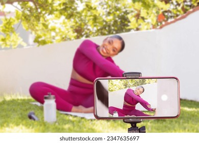 Smartphone screen recording cheerful attractive sporty black woman fitness blogger exercising outdoor at garden. Athletic african american lady fitness coach streaming while stretching body - Powered by Shutterstock