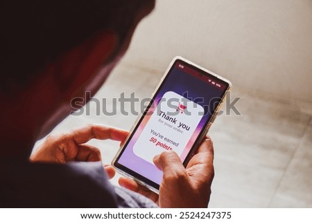 Smartphone screen showing a man earned 50 reward points by shopping online. E-commerce loyalty program concept, selective focus.