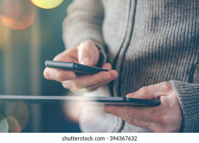 Smartphone and tablet data synchronization, man syncing files and documents on personal wireless electronic devices at home, selective focus with shallow depth of field and bokeh light.