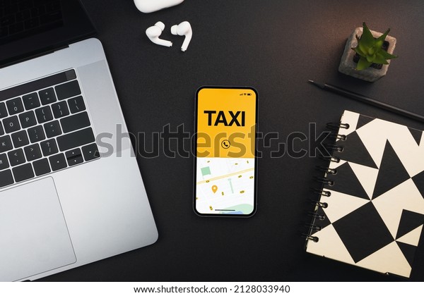 Smartphone with Taxi Service app on the screen\
on black background table. Office environment. Mobility service\
provider worldwide.