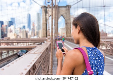 Smartphone Texting Girl On Brooklyn Bridge In Urban New York City, Manhattan USA. View From The Back Of Unrecognizable Business Woman Holding Phone Reading Or Using Social Media In Summer.