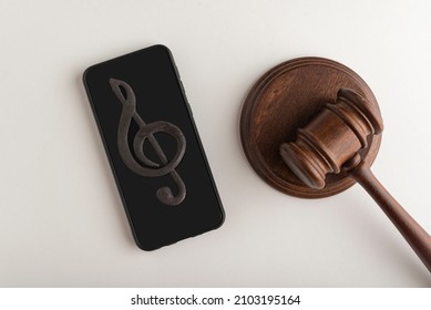 Smartphone with treble clef sign on display and judges hammer. Illegal use of music concept. Digital piracy