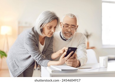 Smartphone usage among older adults, senior couple learn interacting with phone digital information online, nice elderly people, old pair family at home together, keep in touch with family and friends - Powered by Shutterstock