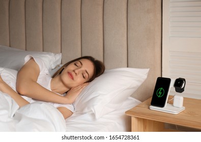 Smartphone, watch, earphones charging on wireless pad and sleeping woman in room - Powered by Shutterstock