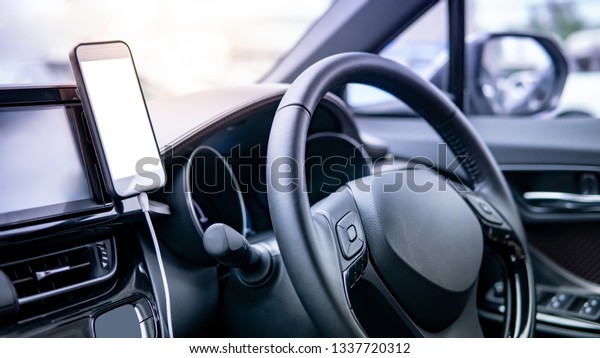 Smartphone with white blank screen mounting\
with magnet on the car console near steering wheel. Using smart\
phone for GPS navigation in modern car. Urban driving lifestyle\
with mobile app\
technology