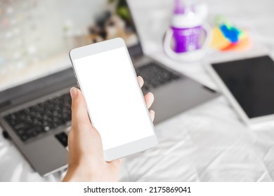 Smartphone With A White Blank Screen On The Background Of An Open Laptop. Working Mom On Maternity Leave Concept. Remote Work For Nursing Mothers