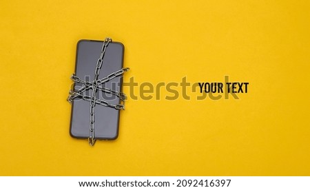 Smartphone wrapped in a steel chain on yellow background. Safety of personal information. Top view
