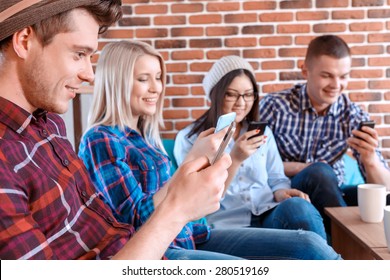 Smartphones rule the world. Young handsome boy and his friends sitting in a cafe. All using their mobile phones instead of talking to each other selective focus