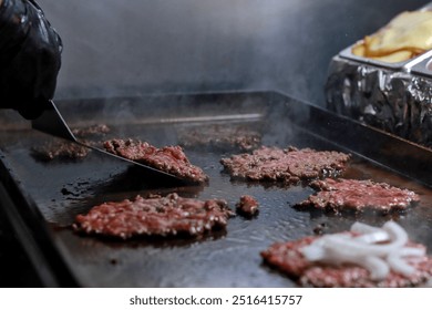 Smash burgers being prepared on a griddle with onions, showing the sizzling cooking process in a professional kitchen - Powered by Shutterstock