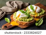 Smashed avocado sandwich with boiled poached egg with flowing  yolk and basil leaves. Dark green background.