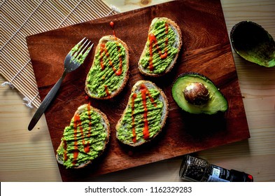 Smashed Avocado Topped With Sriracha Sauce On Toasts