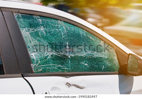 Smashed and cracked side car window glass of\
parked vehicle. Damaged car window. Broken and damaged shattered\
glass of side car window. Criminal incident, broken vehicle side\
window. Street accident