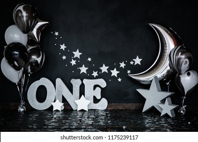 Smashed First Birthday White Cake With Stars And One Candle For Little Baby Boy And Decorations. Black Background. Big Silver Letters ONE, Silver Stars And Different Balloons