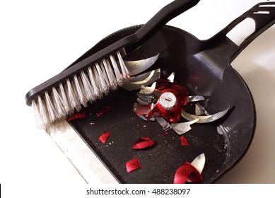 A Smashed Red Holiday Bauble Has Fallen To Many Pieces So A Broom And Dustpan Come To Clean Up The Mess.