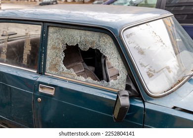 Smashed side window in an abandoned dark green car. Shards of broken glass glass and a broken side mirror