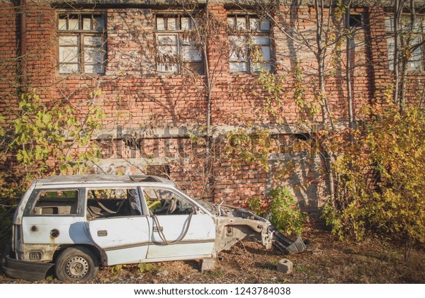 Smashed white car in front of a brick\
house. White damaged car. White car after the\
crush.