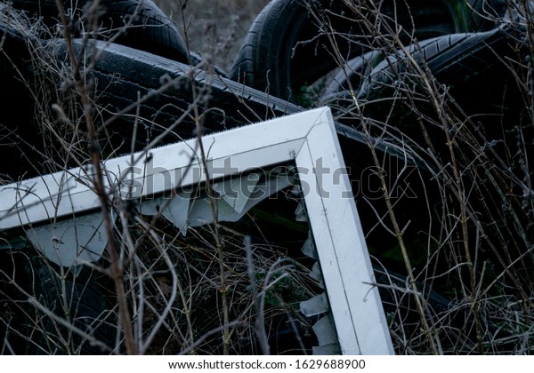 Smashed windows and old tires\
dumped in a field. Industrial waste / rubbish background. UK rural\
crime.