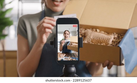SME owner go green net zero retail store live stream talk on phone showing eco care plastic free packaging box. Asia people young woman record video on tiktok IG reel instagram shop happy side hustle.