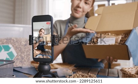 SME owner go green net zero retail store live stream talk on phone showing eco care plastic free packaging box. Asia people young woman record video on tiktok IG reel instagram shop happy side hustle. [[stock_photo]] © 