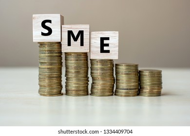 SME ( Small Medium Enterprise) Wooden Cube With Golden Coin On Growing Money Stairs Or Stack On  Table. Business, Investment, Retirement Planning, Finance And Saving For The Future Concepts