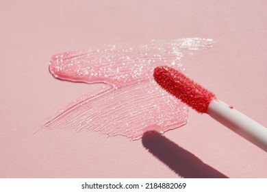 Smears Of Shining Lip Gloss And Lip Gloss Brush On Pink Background, Hard Shadows