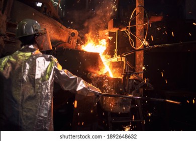 Smelting of metal in large foundry. Iron and steel being melted in furnace. Worker controlling metallurgy process of molten iron. Hot steel pouring in production plant. - Powered by Shutterstock