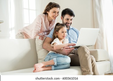 smiing parents and focused daughter using laptop at home
