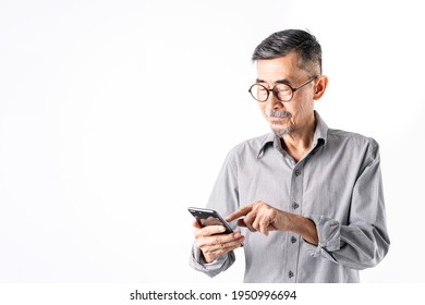 A Smile Asian Elder Man In A Gray Shirt Uses A Cell Phone For Texting Or Online Social Media. White Background In A Studio. Positive Active Old Cool Senior Technology Retirement Concept. Copy Space.