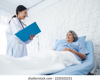 Smile Asian senior woman grey hair patient lying on bed, recovering while young female doctors visit, explaining the symptoms and examination notes and medical healthcare documents in hospital room.  - Powered by Shutterstock