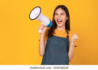 Smile Asian woman wear apron and holding megaphone with fists clenched celebrating victory expressing success on yellow background. - Powered by Shutterstock