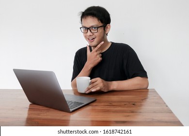 Smile Face And Funny Tricky Awkward Smirk Face Of Young Asian Man With Hand In Chin In A Black T-shirt In A Front Of A Laptop.