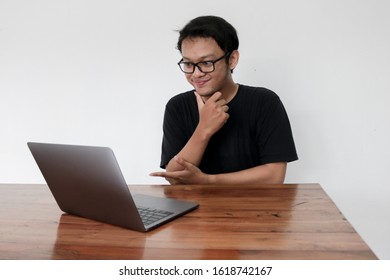 Smile Face And Funny Tricky Awkward Smirk Face Of Young Asian Man With Hand In Chin In A Black T-shirt In A Front Of A Laptop.