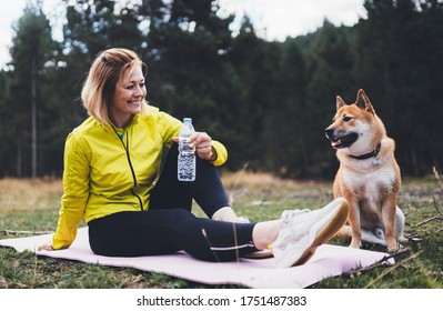 Smile Girl With Pet Together Relax After Exercising Outdoors On Yoga Mat, Shiba Inu Dog On Nature, Isolation Fitness Woman Drink Water From Thirst Training Outside. Healthy Lifestyle Concept