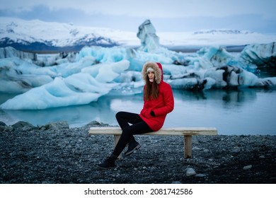 Smile Girl Sitting On Bench In Jokulsarlon Glacier Lagoon In Iceland. Sustainable Travel Concept. Tourist Offset Carbon Footprintto Battle Climate Change, Global Warming. Woman On Iceland Nature