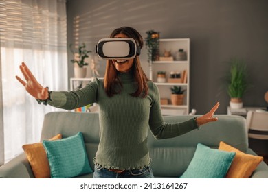 Smile happy woman getting experience while using VR headset glasses of virtual reality at home and gesticulating with hands while exploring space. Modern technology leisure concept. - Powered by Shutterstock