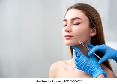 Smile lifting and lip augmentation. Beautician doctor hands doing beauty procedure to female face with syringe. Young woman's mouth countouring with filler injection. Marionette lines treatment. - Shutterstock ID 1407664622