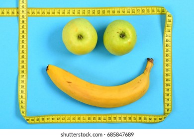 Smile Made Of Banana And Green Apples Framed With Yellow Flexible Ruler Isolated On Cyan Blue Background. Concept Of Happiness And Food Art