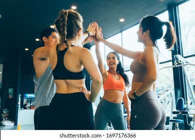 Smile Man And Women Making Hands Together In Fitness Gym. Group Of Young People Doing High Five Gesture In Gym After Workout. Happy Successful Workout Class After Training. Teamwork Concept