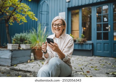 smile mature woman owner waitress sit in front restaurant and use mobile phone