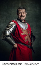 Smile. Portrait Of Smiling Man In Image Of Medieval Warrior With Wounded Face Wearing Equipment Isolated Over Dark Background. Comparison Of Eras, History, Renaissance Style. Funny Meme Emotions