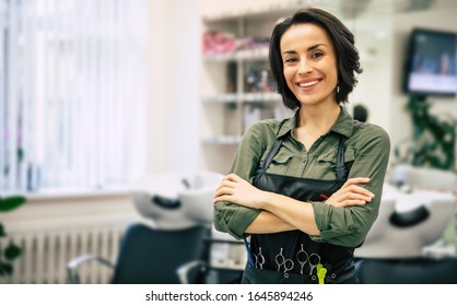Smile of the professional. Portrait of a gorgeous young hairstylist standing with folded arms near her workplace in the salon.