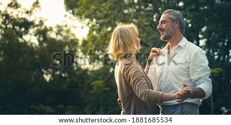 Smile Senior romantic couple dancing and looking each other feeling love and cherish on their anniversary in the park, happily senior citizen, well-managed retired life concept. Married lifestyle.
