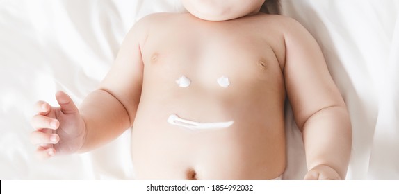 Smile Sign On A Baby's Belly Painted With A Cream. Baby Lying On A White Blanket. No Face Visible. Close Up.