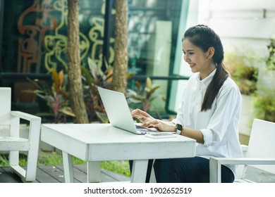 Smile Woman Is Chat With Someone’s The Garden Or Outside Of The Cafe. She Is Typing The Document On The Laptop While She Sitting On The Outdoors Seat.