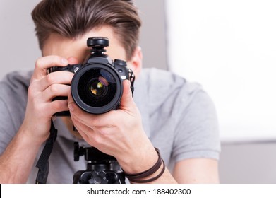 Smile! Young man focusing at you and digital camera while standing in studio and lighting equipment background 