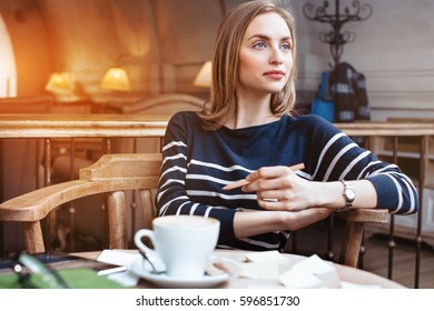 A smile young woman dreams seat in a cafe with cup of coffee with wooden pencil in hand. Concept of planning personal training schedule.Looking away.