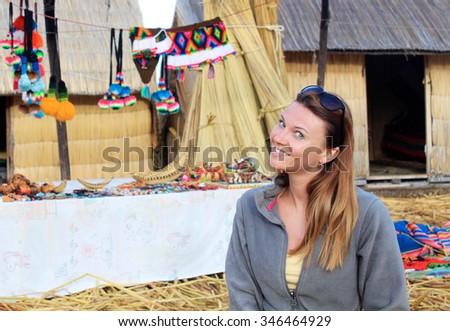A smiled woman sits on the ground of floating island Uros in the lake Titicaca in Peru, bright different colour Peruvian handcraft souvenirs are on the background of the photo