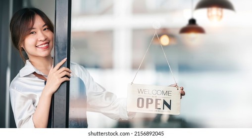 Smiley Asian Female Barista Holding Open Board Sign Standing At Her Shop.